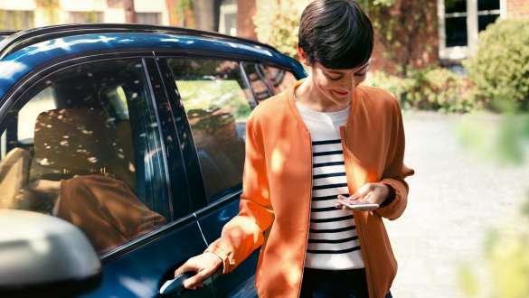 BMW Teleservices BMW Teleservices vrouw met smartphone bij portier van BMW