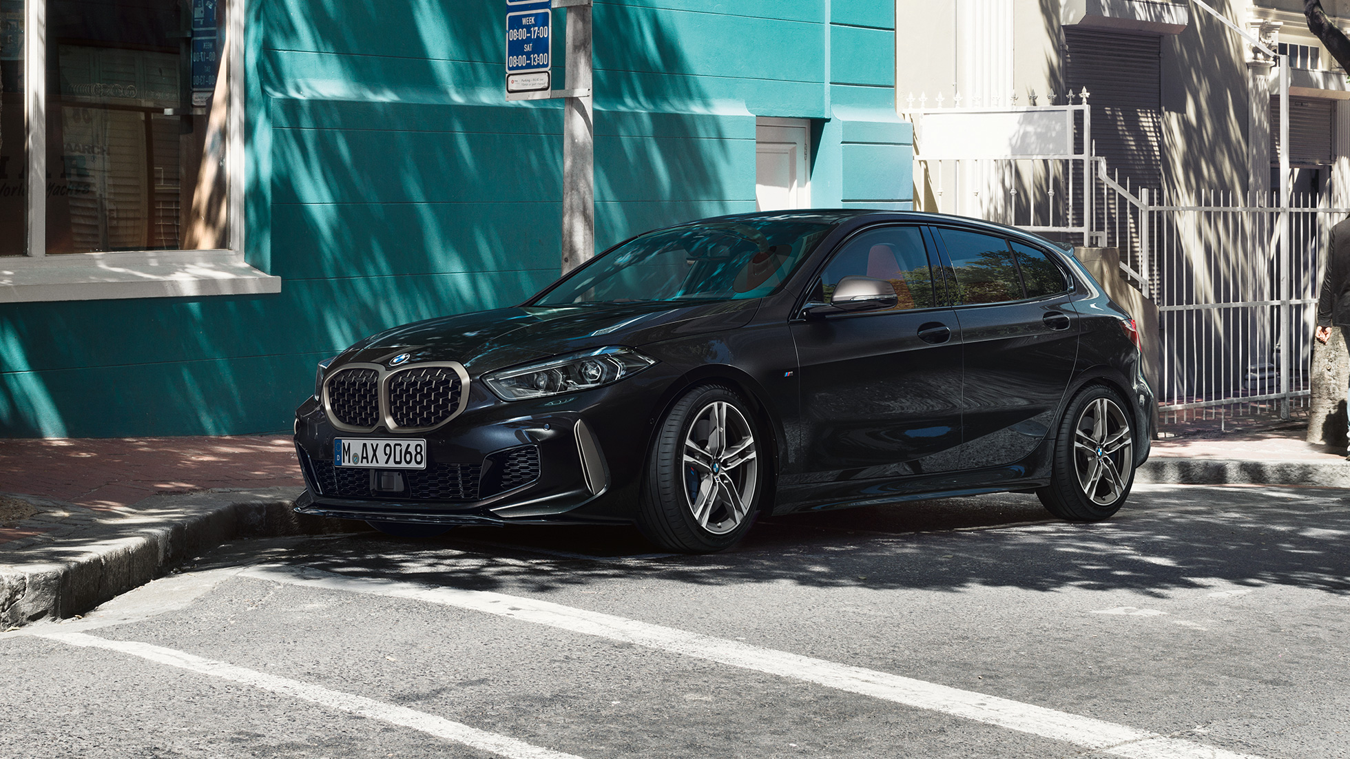 BMW M135i xDrive, driekwart zijaanzicht. BMW M135i xDrive in Saphirschwarz metallic, driekwart zijaanzicht parkerend.