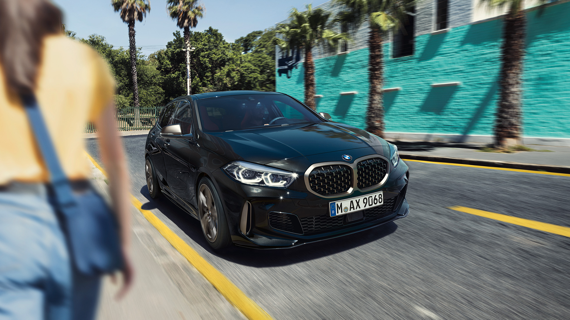 BMW M135i xDrive, driekwart vooraanzicht. BMW M135i xDrive in Saphirschwarz metallic, driekwart vooraanzicht rijdend.