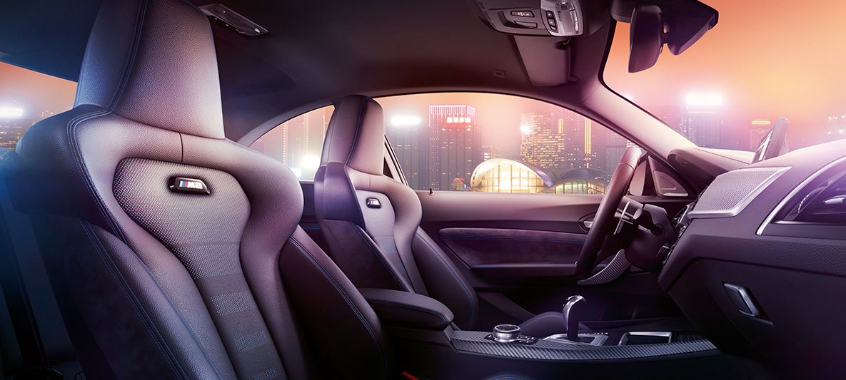 BMW M2 Competition sportstoelen Cockpit en M sportstoelen van de BMW M2 Competition met een nachtelijke skyline op de achtergrond.