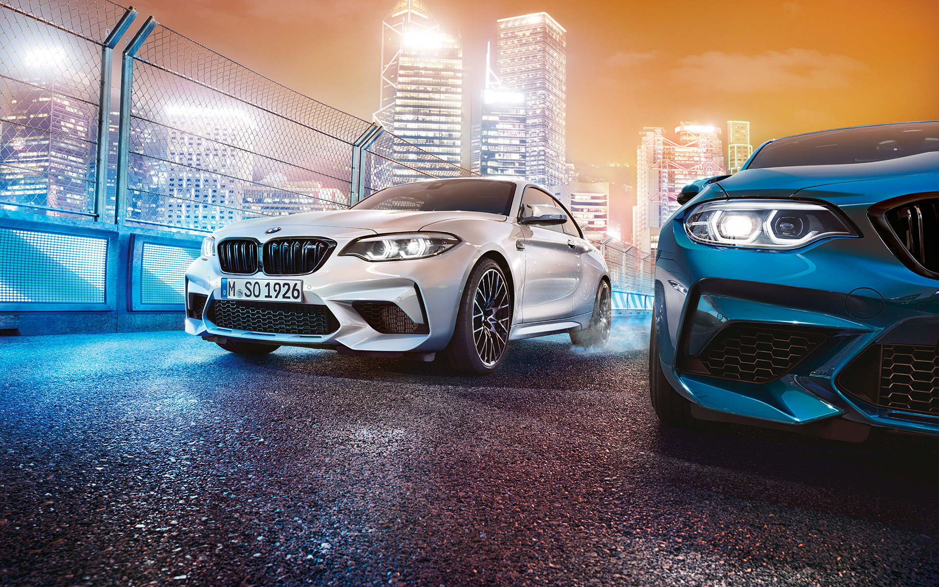 BMW M2 Competition vooraanzicht Witte en blauwe BMW M2 Competition van voren gezien met op de achtergrond een nachtelijke skyline.