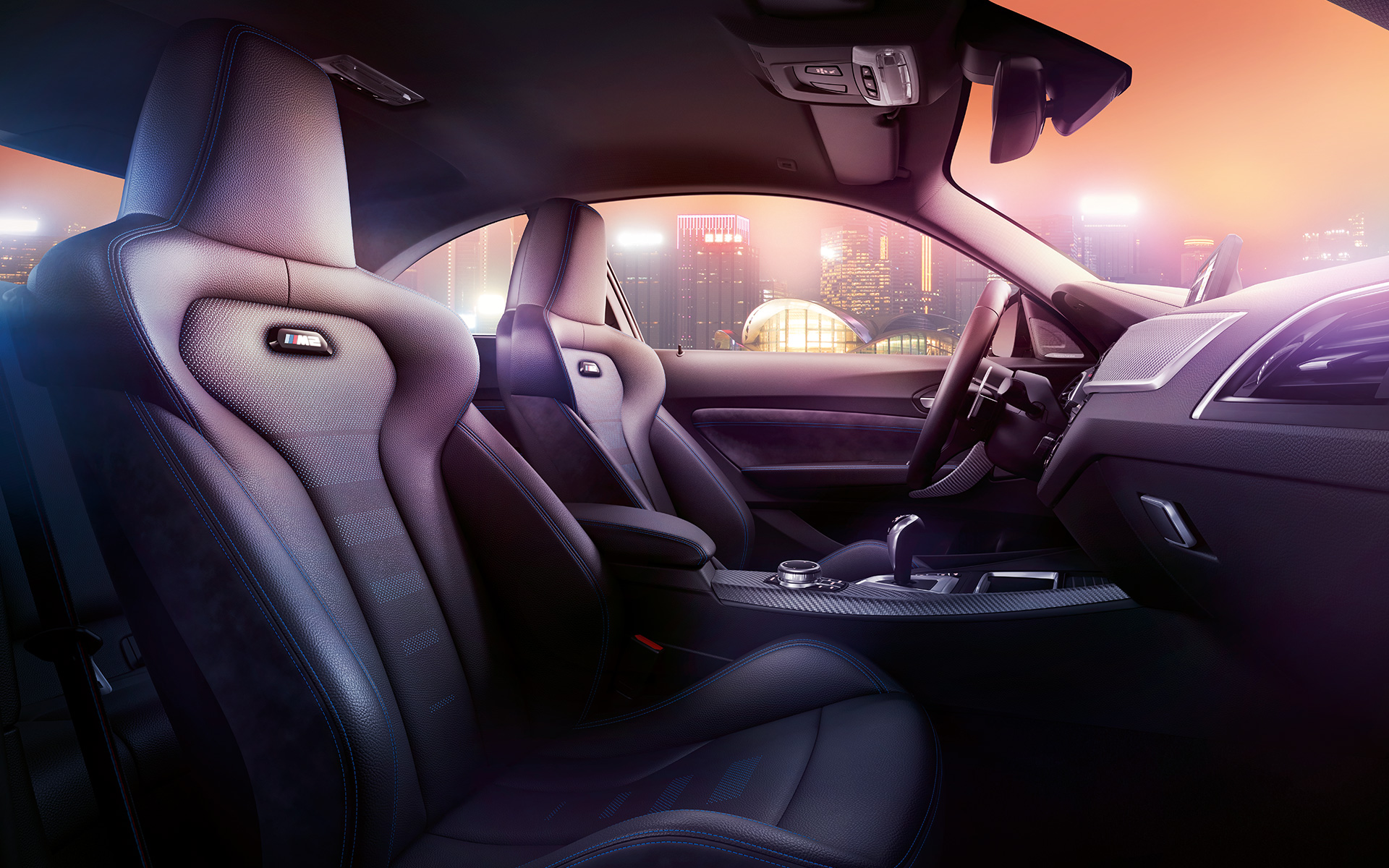 BMW M2 Competition sportstoelen Cockpit en M sportstoelen van de BMW M2 Competition met een nachtelijke skyline op de achtergrond.