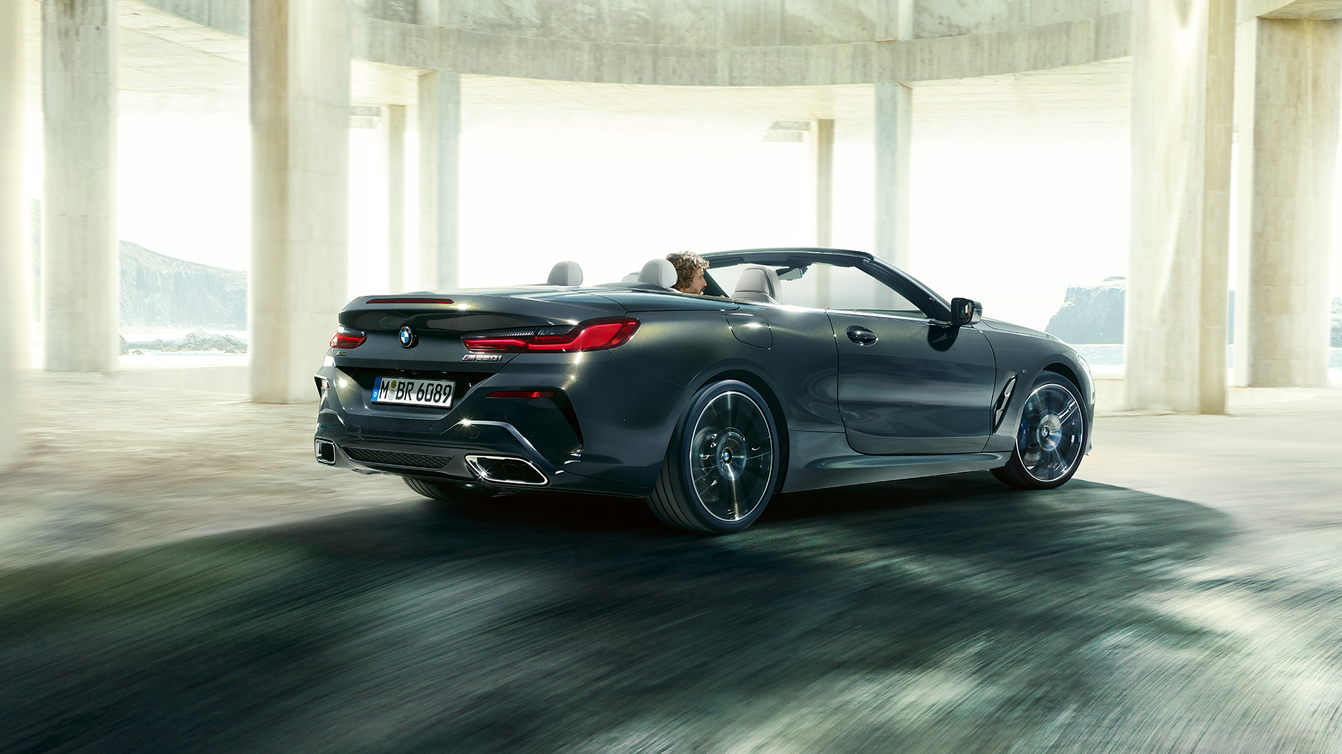 BMW M850i xDrive Cabrio, driekwart achteraanzicht. BMW M850i xDrive Cabrio in Dravitgrau metallic, met geopende softtop, driekwart achteraanzicht, rijdend