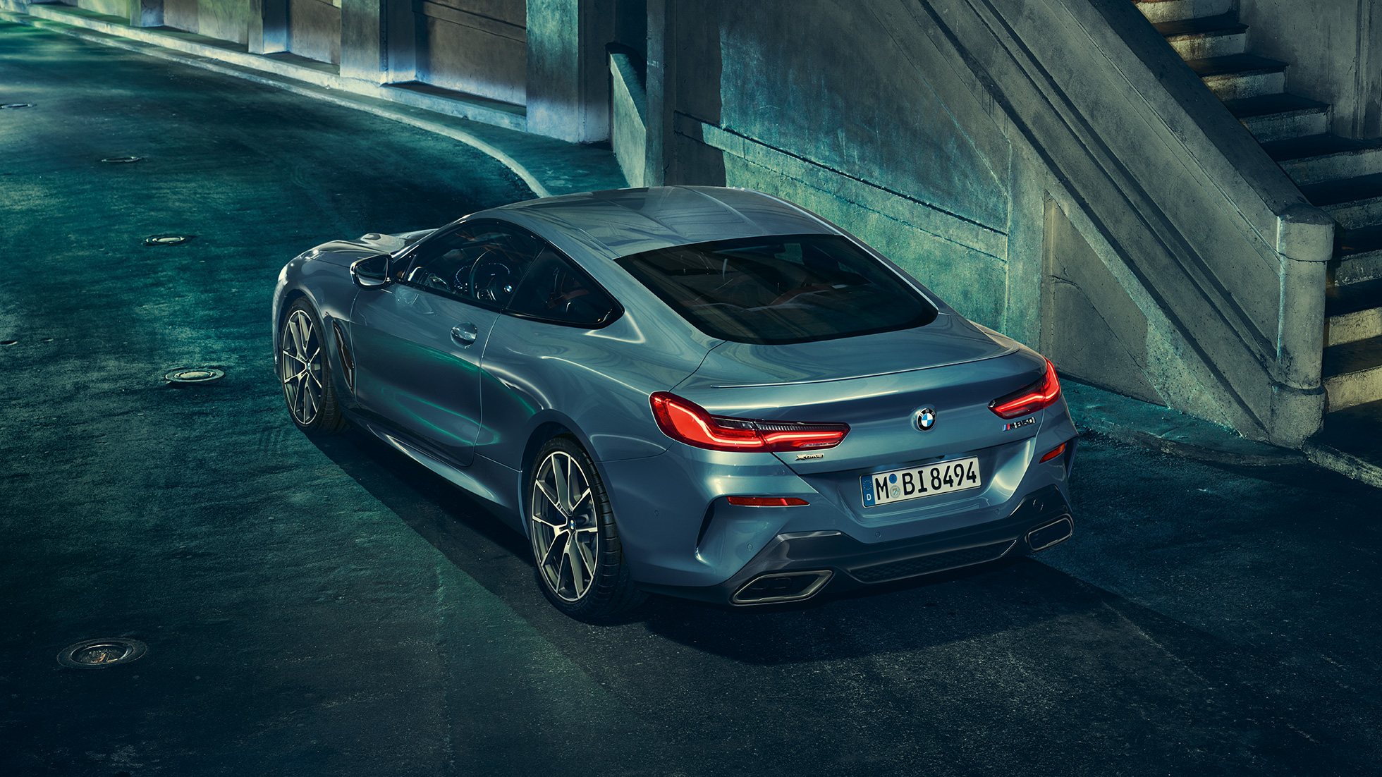 BMW M850i xDrive Coupé, driekwart achteraanzicht links. BMW M850i xDrive Coupé in Barcelona Blau metallic, driekwart achteraanzicht links.