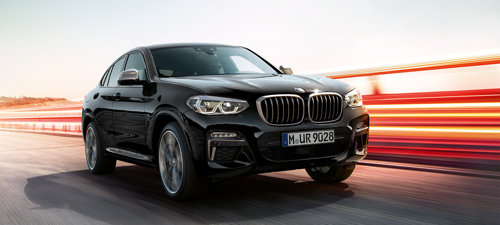 BMW X4 M40i en BMW X4 M40d, driekwart vooraanzicht links. BMW X4 M40i en BMW X4 M40d in Saphir Schwarz metallic, rijdend, exterieur, driekwart vooraanzicht.