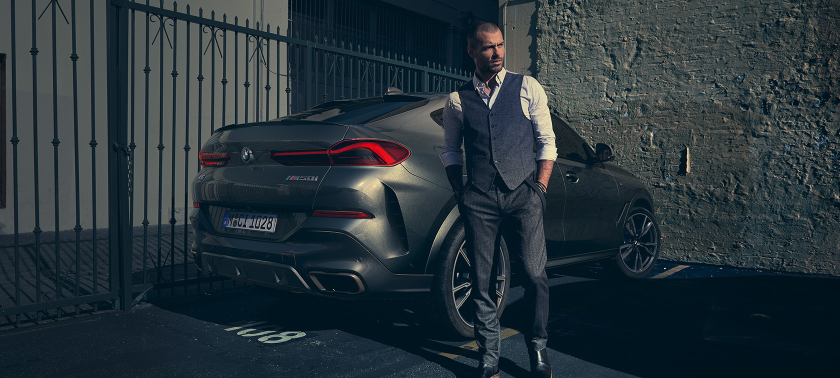 BMW X6 M M50i G06 driekwart achteraanzicht Man naast BMW X6 M M50i G06 SUV driekwart achteraanzicht