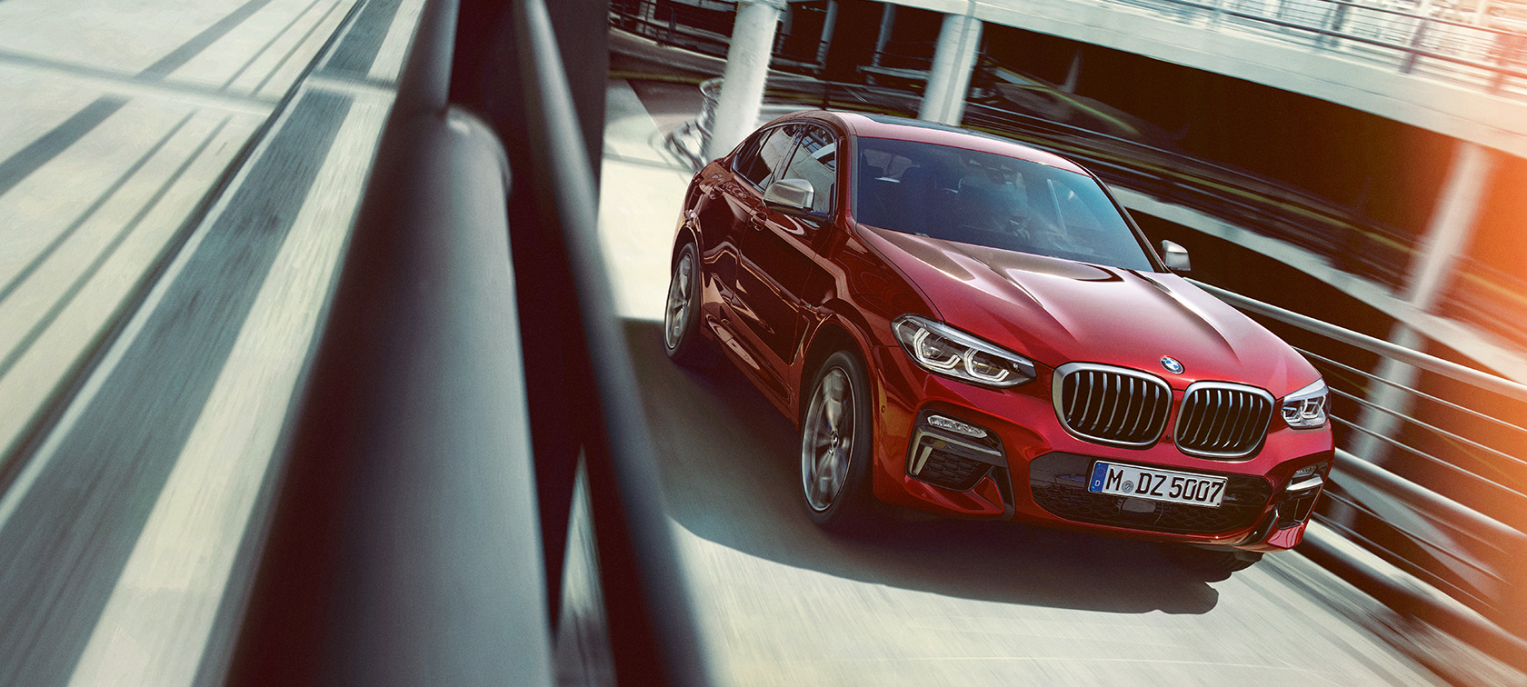 BMW X4 rijdend in parkeergarage BMW X4 G02 2018 Flamencorot Brillanteffekt driekwart zijaanzicht rijdend in parkeergarage