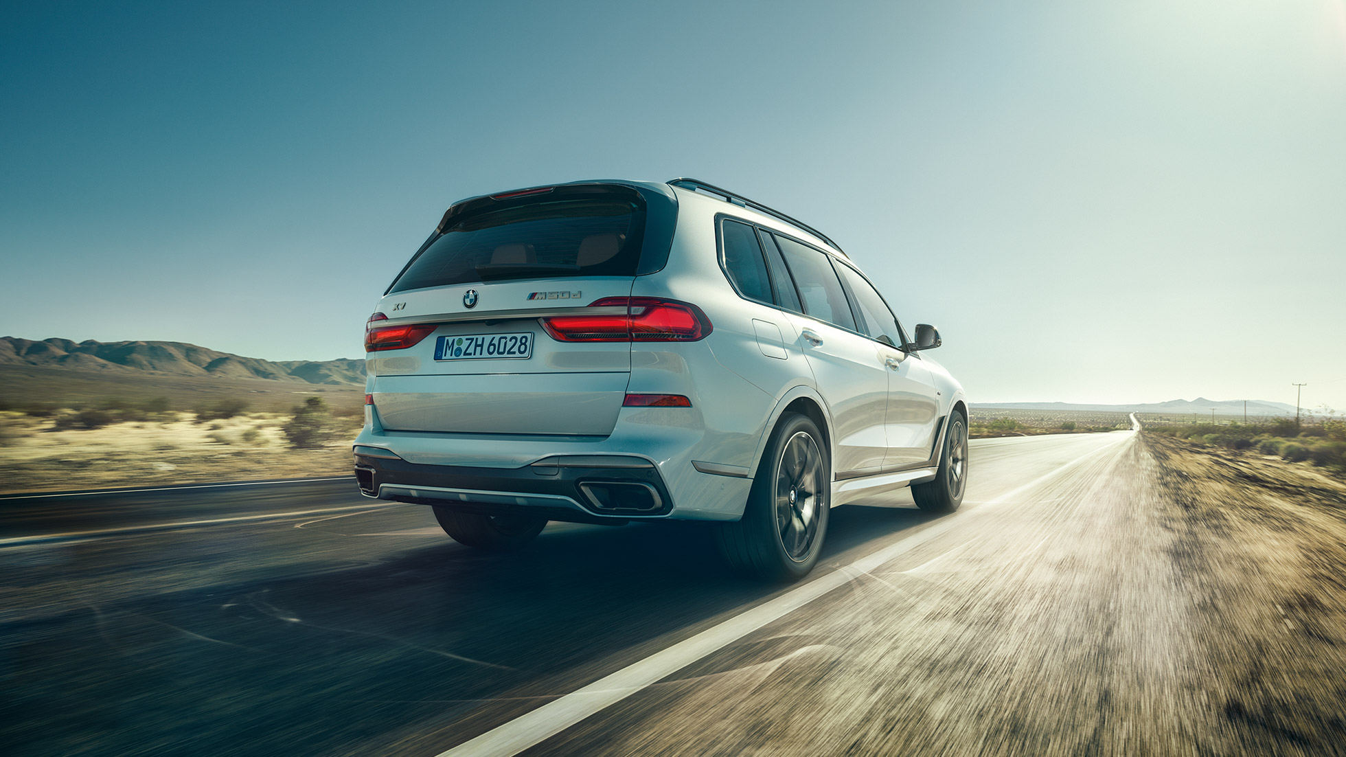 BMW X7 M50d, achteraanzicht BMW X7 M50d: achteraanzicht van een rijdende, witte BMW X7