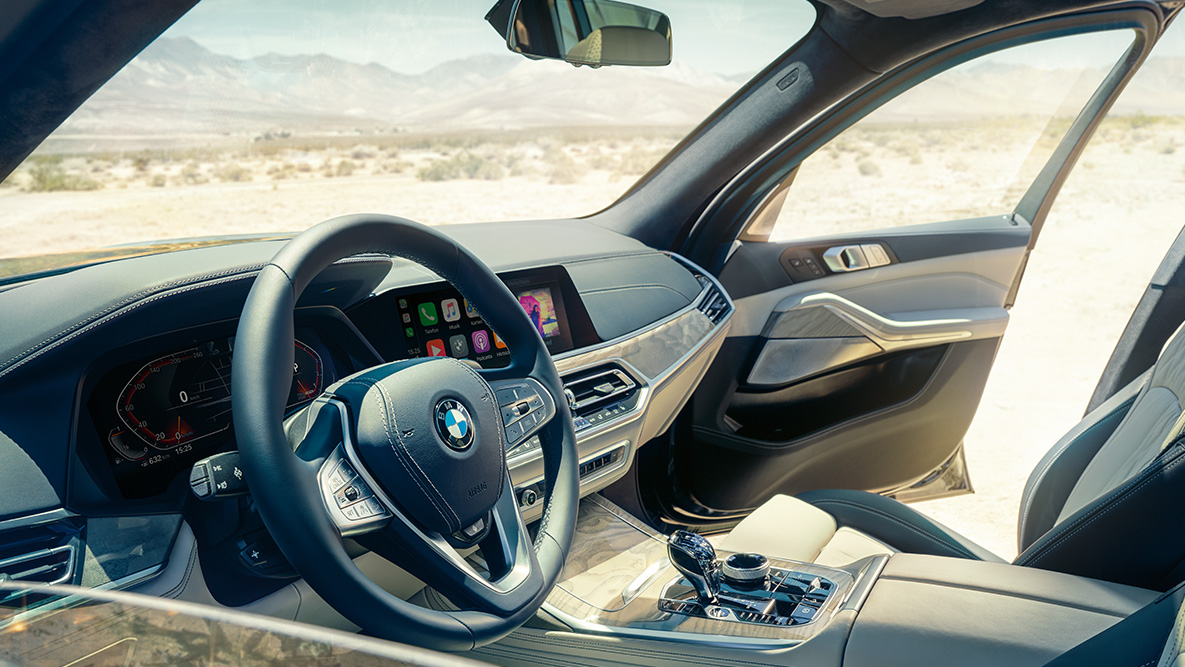 BMW X7 interieur BMW X7 interieur: aanzicht van buitenaf op de eerste zitrij met zicht op stuur, instrumentenpaneel en met leder beklede stoelen