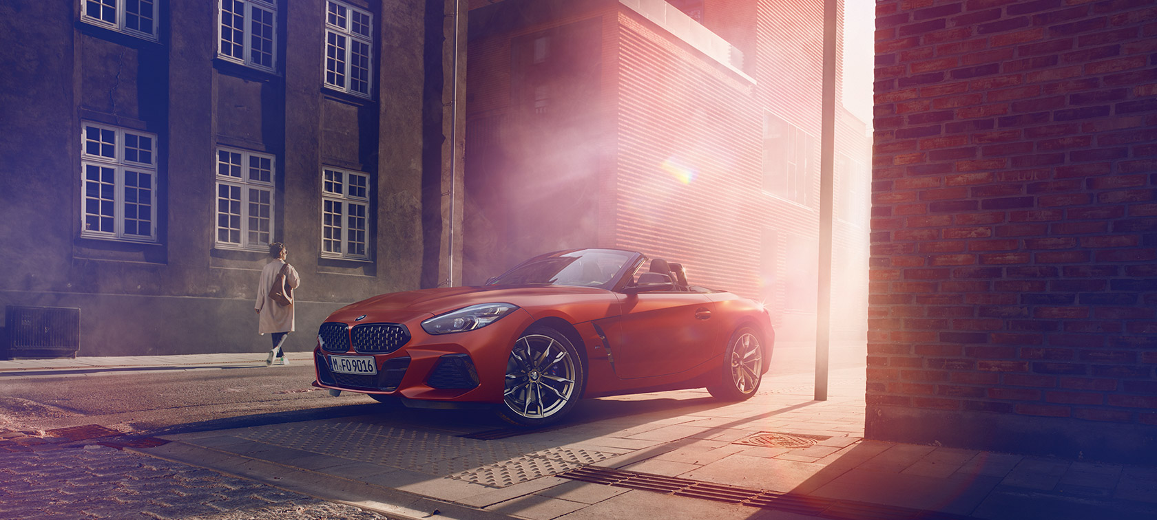 Oranje BMW Z4 First Edition op de weg Oranje BMW Z4 First Edition op een halfverlichte weg voor huizen met vrouw