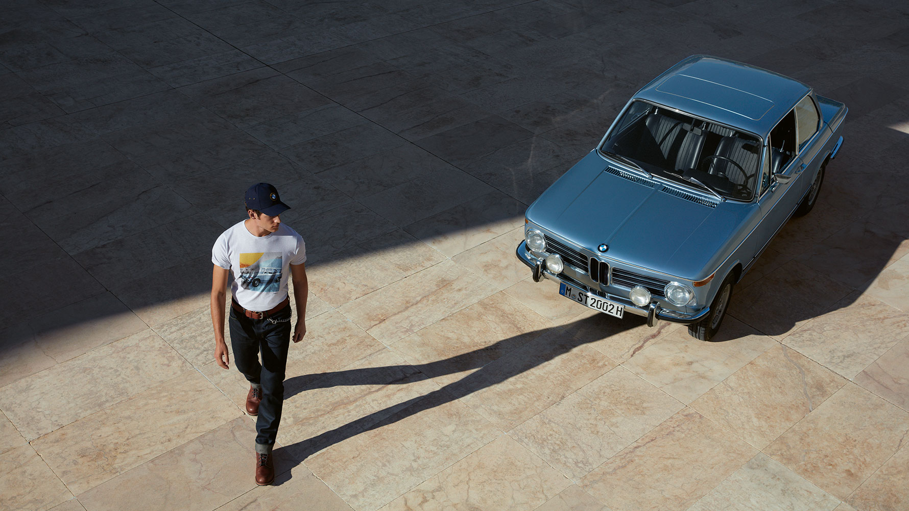 Een man draagt een BMW Classic T-shirt voor heren uit de BMW Classic Collection en bewondert een BMW oldtimer Een man draagt een BMW Classic T-shirt voor heren uit de BMW Classic Collection en bewondert een BMW oldtimer