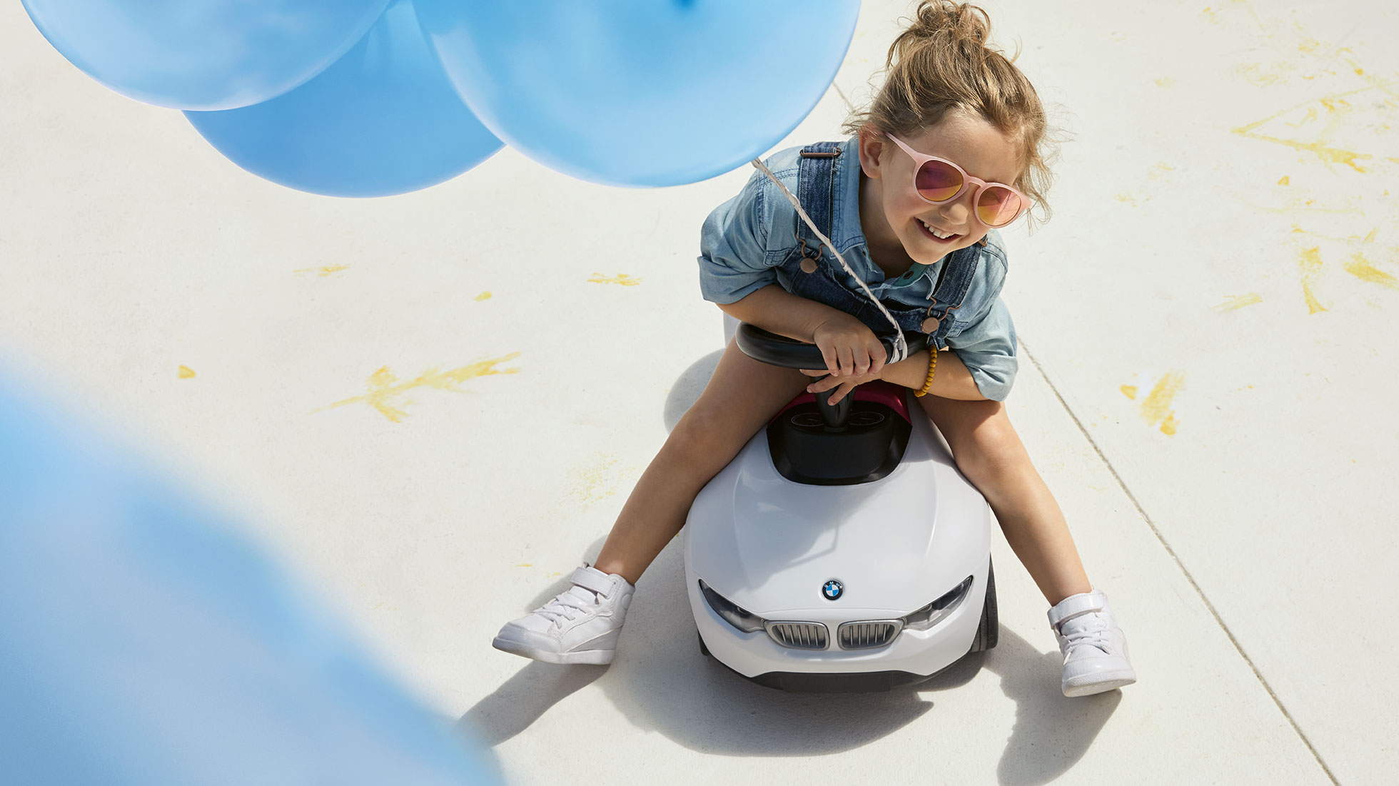 BMW Kids Collection Een meisje zit vrolijk op een BMW Babyracer