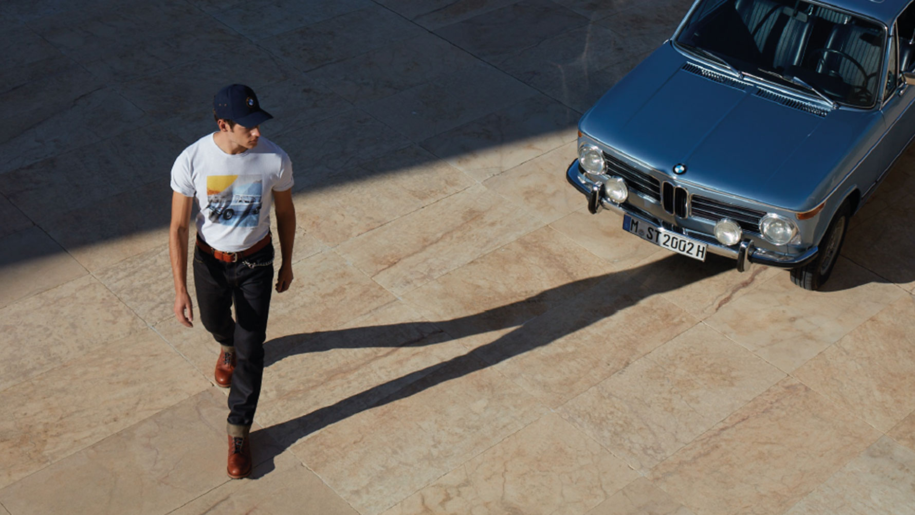 Een man draagt een BMW Classic T-shirt heren uit de BMW Classic Collection en bewondert een BMW oldtimer. Een man draagt een BMW Classic T-shirt heren uit de BMW Classic Collection en bewondert een BMW oldtimer.