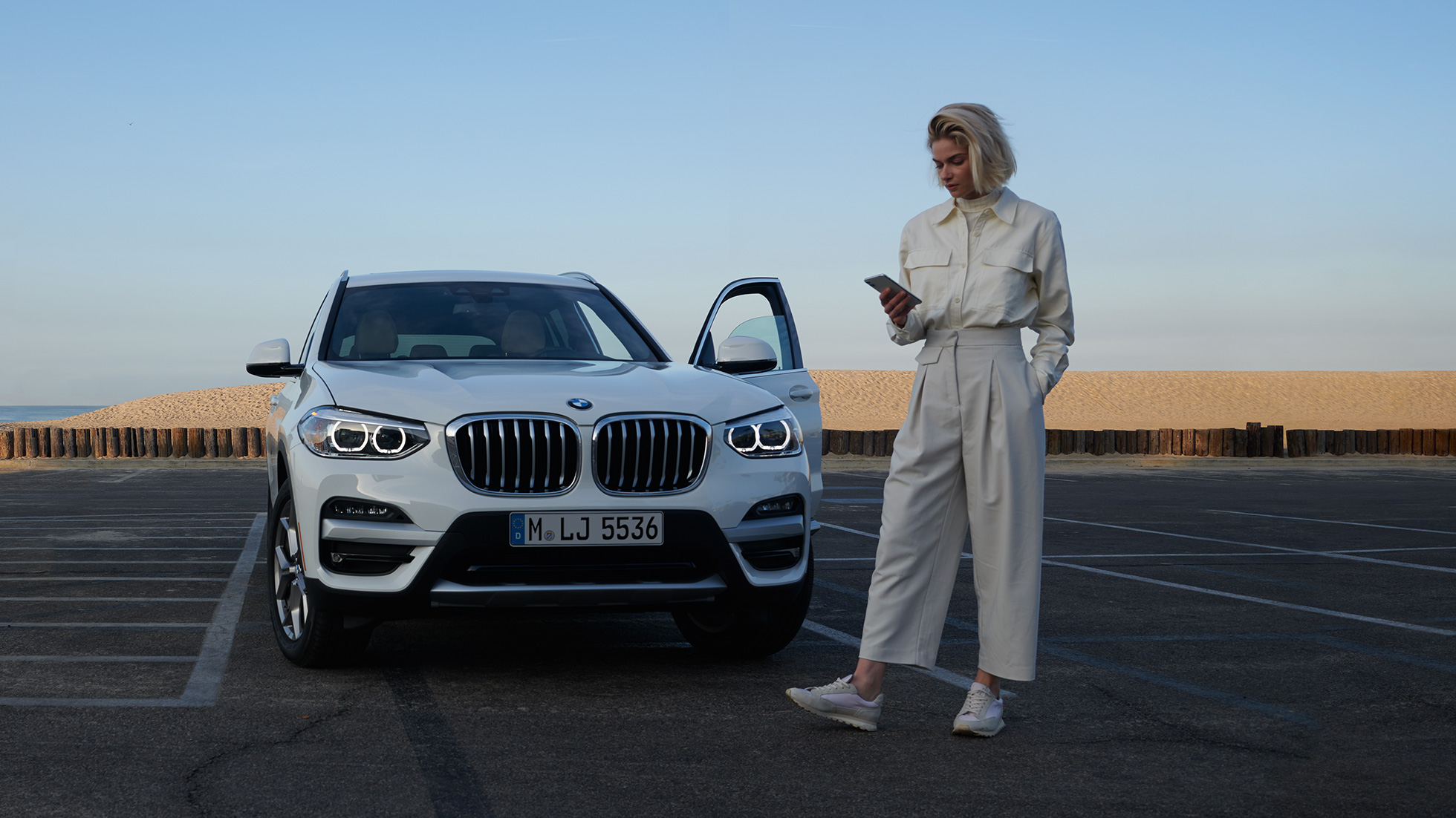 Vrouw gebruikt My BMW App op smartphone Vrouw gebruikt My BMW App van BMW ConnectedDrive op de smartphone voor BMW X5