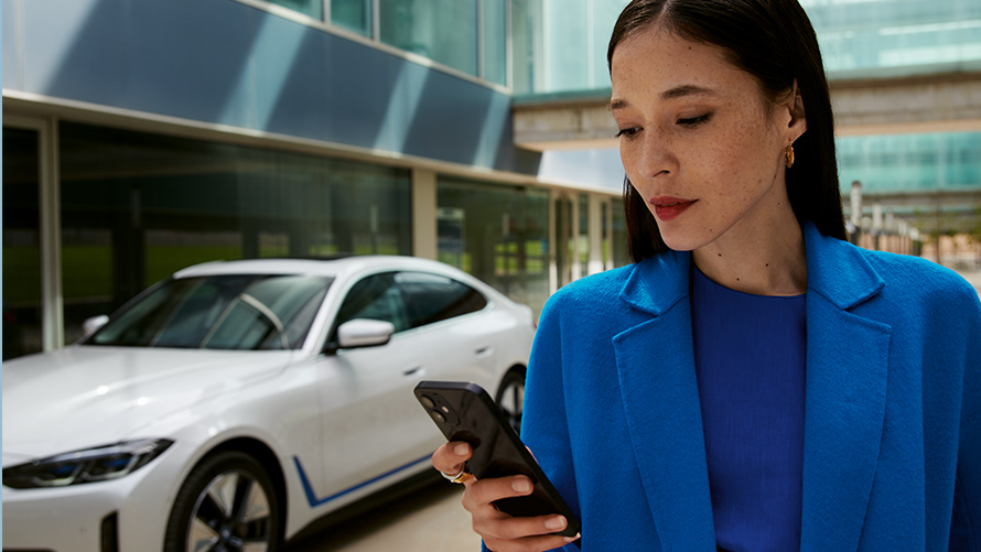 Vrouw staat voor een BMW Vrouw op brug voor een BMW kijkt op smartphone