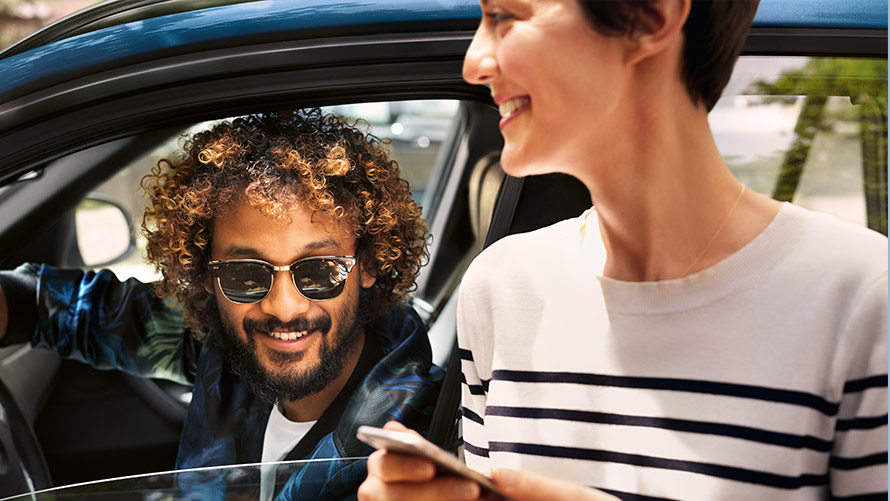 My BMW App Man in BMW en vrouw naast BMW gebruiken de My BMW App op de smartphone
