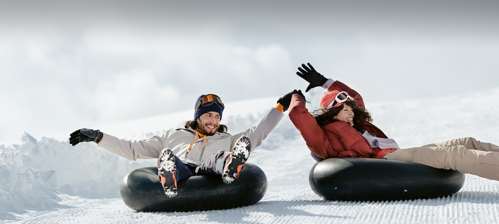 Originele BMW Accessoires en BMW Service voor herfst en winter Vrouw en man lachend op rodelband in sneeuw