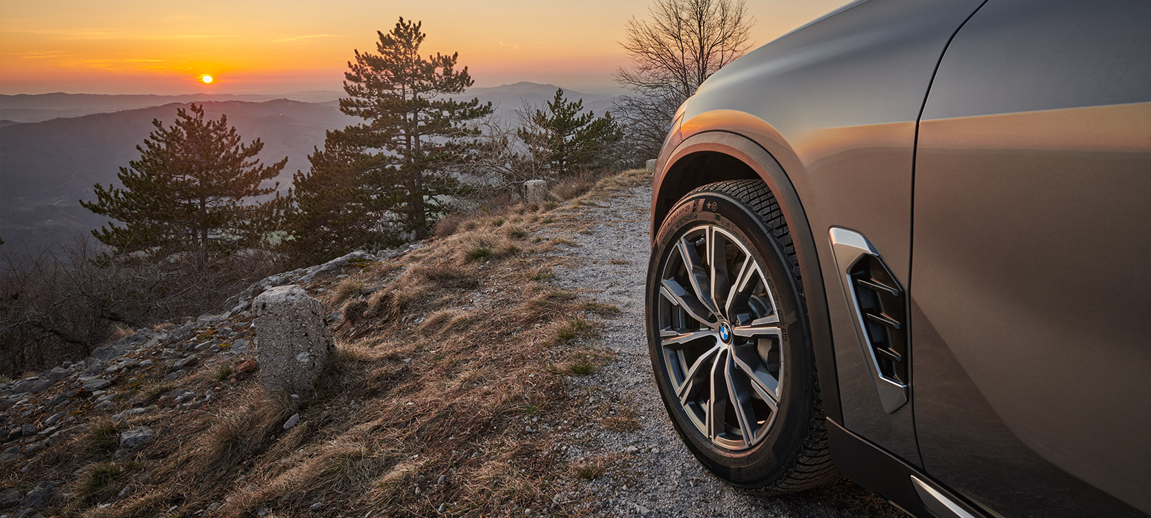 Originele BMW wielen op BMW X5 (G05 LCI) Originele BMW wielen op de BMW X5 (G05 LCI) op weg in berglandschap met zonsondergang