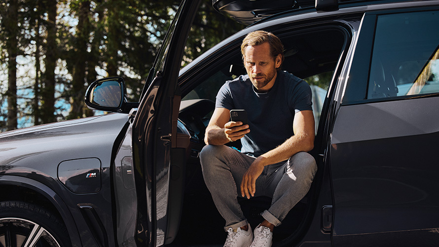 Man in BMW kijkt op smartphone BMW lente- en zomeraccessoires man in BMW kijkt op smartphone