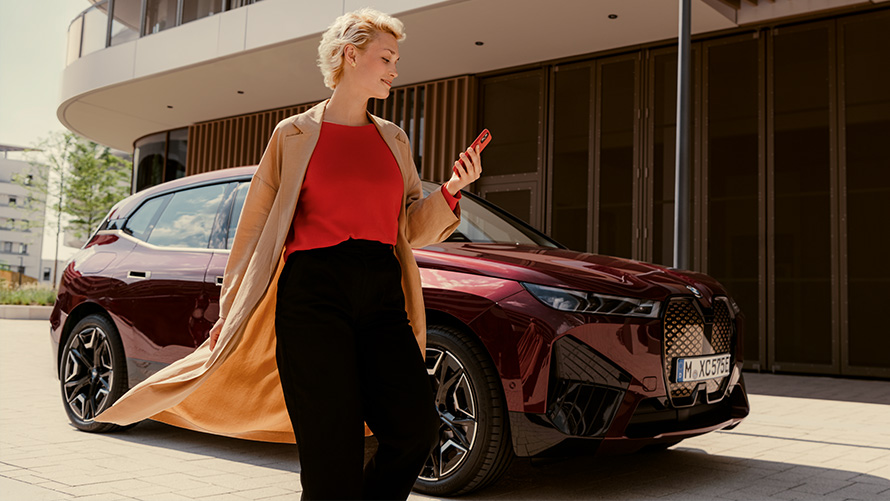 My BMW App My BMW App BMW iX i20 vrouw loopt met smartphone in de hand langs BMW