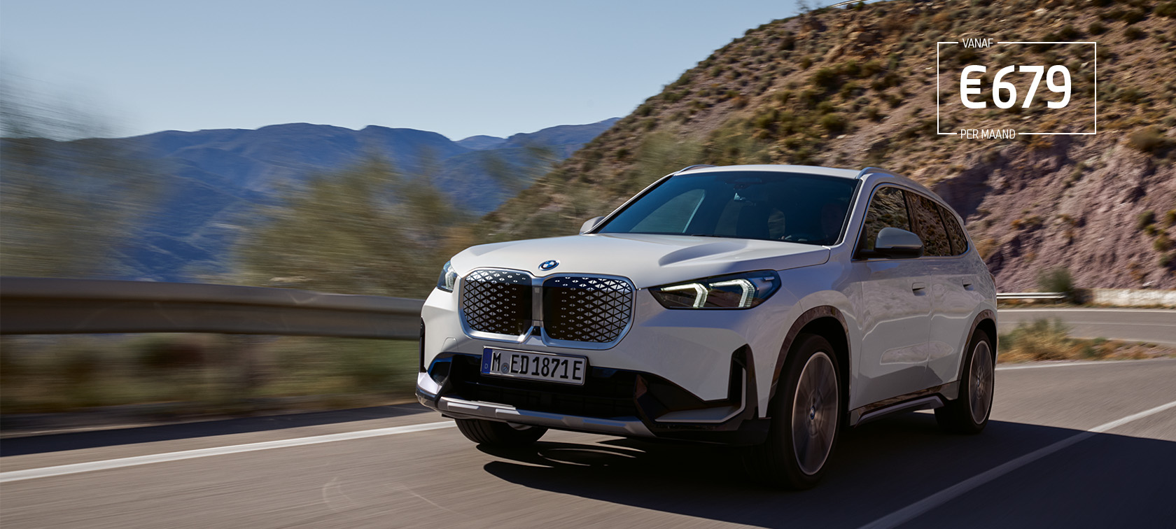 BMW iX1 U11 BEV Mineralweiß metallic driekwart vooraanzicht rijdend op bochtige bergweg