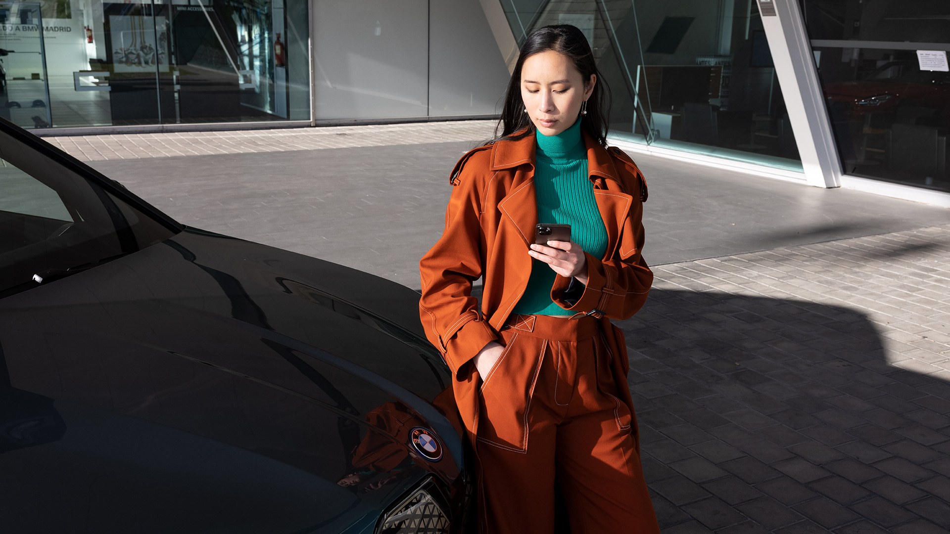 Vrouw naast BMW met smartphone.
