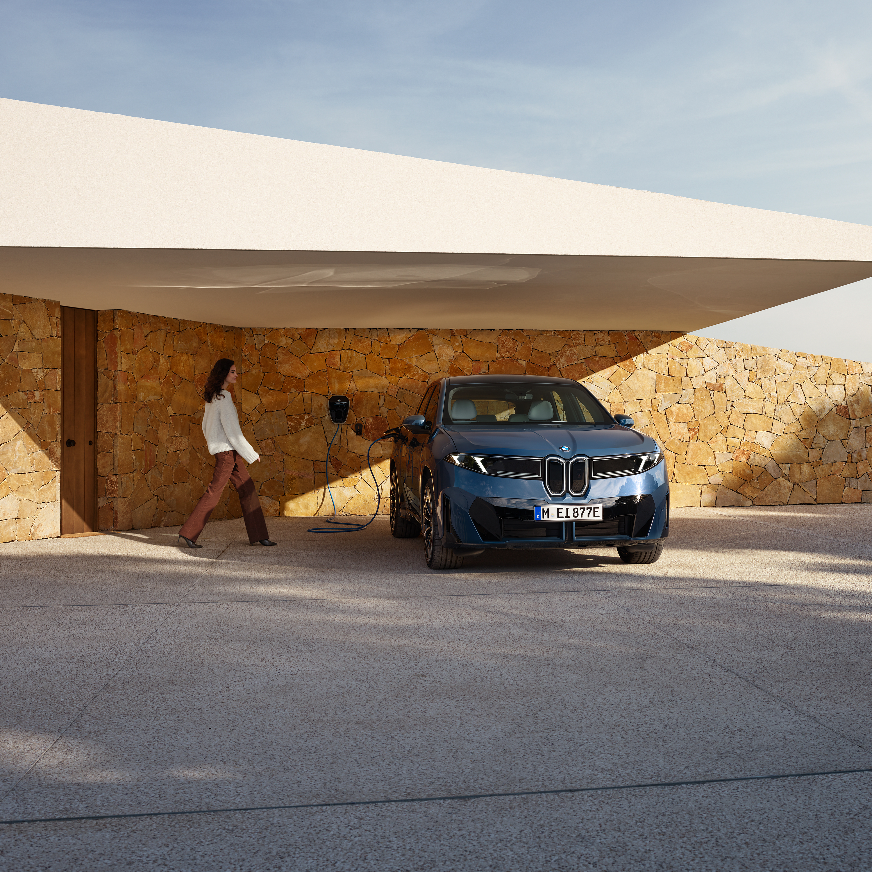 Een dame loopt naar een BMW iX3 die is aangesloten op een wallbox
